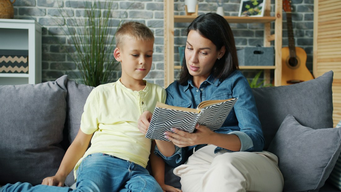 An adult and child reading together on a sofa